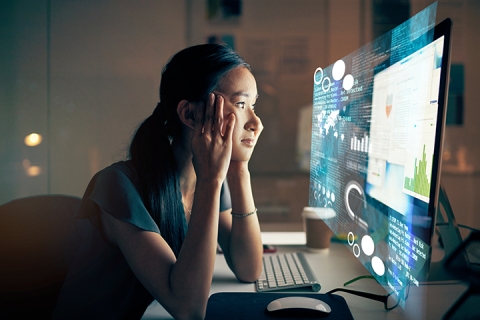 young woman looking at her computer screen late at night experiencing fatigue