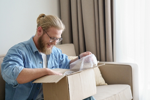 young man smiling and opening a box in his living room