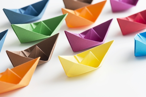 Multi coloured paper boats on white background.