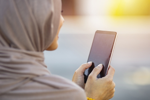 Female wearing hijab texting on cellphone on urban street