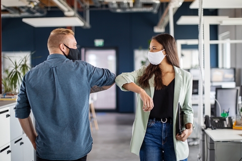 Two business colleagues wearing masks greeting with elbow in office