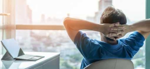 Man looking out the window with his hands placed behind his head