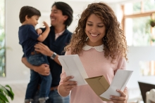 young mother looking at the mail while dad and son play at background all smiling