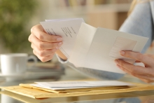 Close up of girl hands opening an envelope with a letter inside on a desk at home